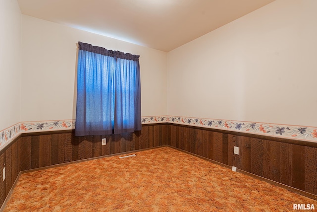 empty room with carpet flooring, lofted ceiling, and wood walls