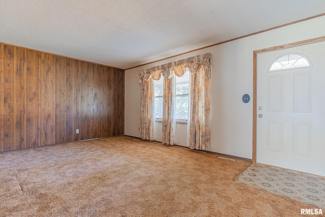 foyer entrance with a wealth of natural light, wood walls, a textured ceiling, and light colored carpet