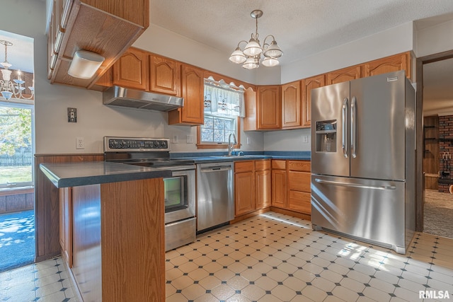 kitchen featuring stainless steel appliances, kitchen peninsula, a textured ceiling, a chandelier, and decorative light fixtures