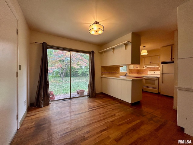 kitchen featuring dark hardwood / wood-style flooring, kitchen peninsula, sink, backsplash, and white appliances