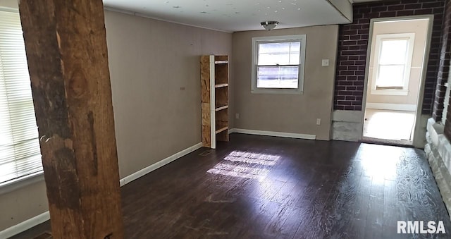 spare room with dark wood-type flooring and brick wall