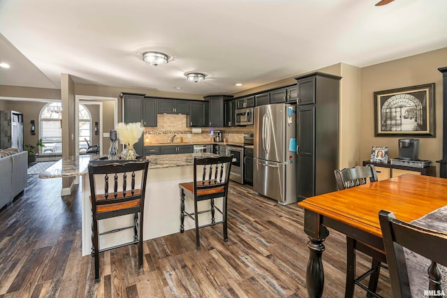 kitchen with dark wood-type flooring, sink, appliances with stainless steel finishes, tasteful backsplash, and a breakfast bar area