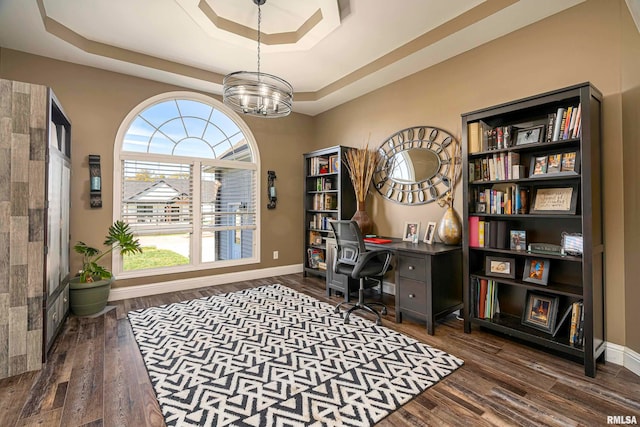 home office with a tray ceiling, dark wood-type flooring, and an inviting chandelier