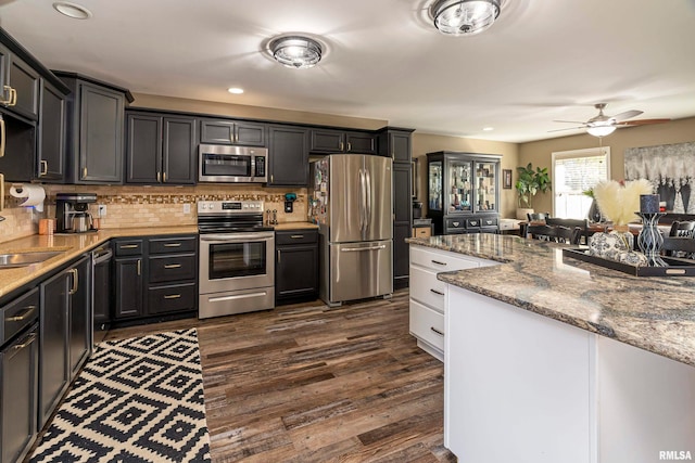 kitchen with backsplash, dark hardwood / wood-style floors, ceiling fan, light stone countertops, and appliances with stainless steel finishes