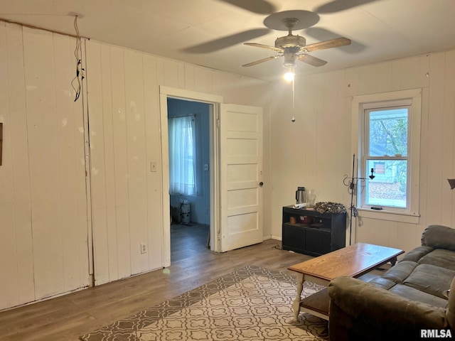 living room featuring wood-type flooring, ceiling fan, and wood walls