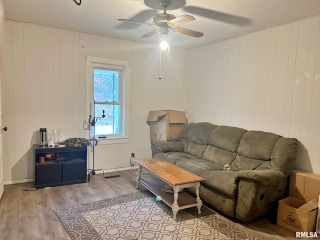 living room featuring ceiling fan, light hardwood / wood-style floors, and wooden walls