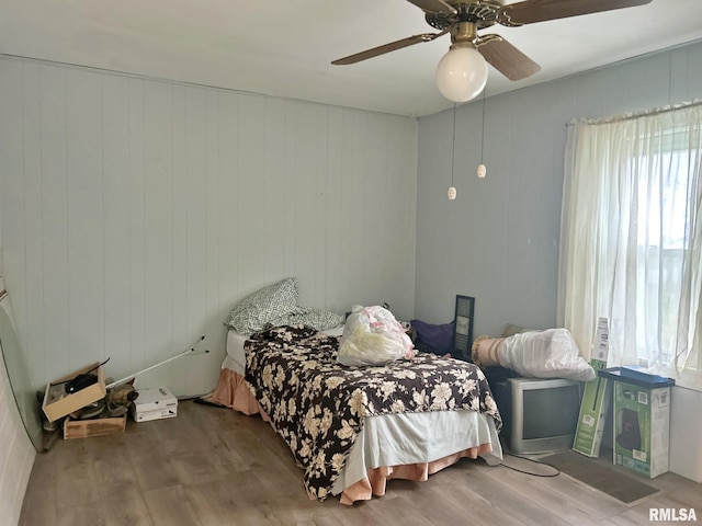 bedroom with hardwood / wood-style flooring, ceiling fan, and wooden walls