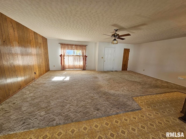 carpeted empty room featuring ceiling fan, wooden walls, and a textured ceiling