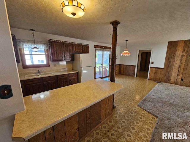 kitchen featuring sink, white refrigerator, wooden walls, and a healthy amount of sunlight