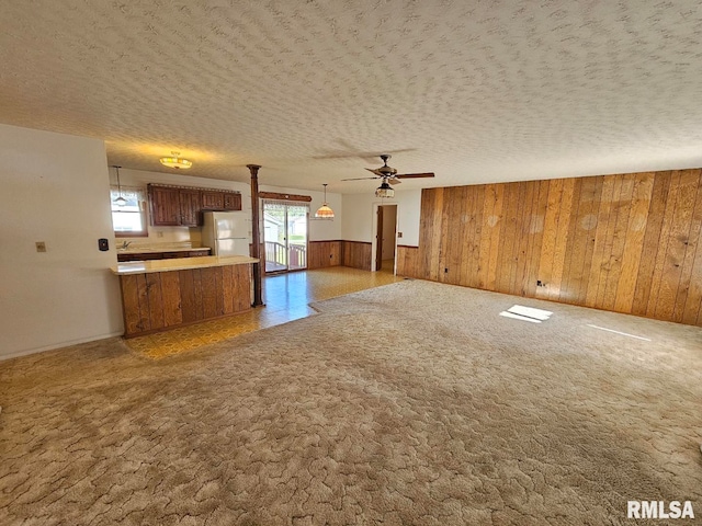 unfurnished living room featuring a textured ceiling, wood walls, ceiling fan, and light carpet