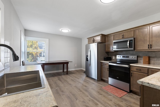 kitchen with decorative backsplash, light wood-type flooring, appliances with stainless steel finishes, and sink