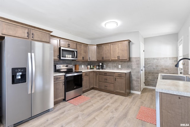 kitchen with appliances with stainless steel finishes, sink, and light hardwood / wood-style floors