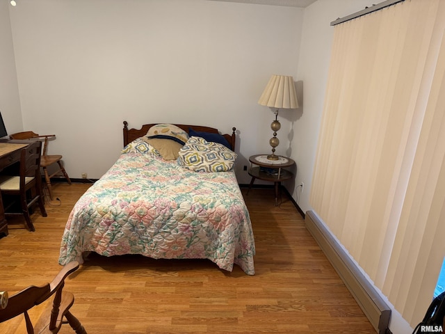 bedroom featuring a baseboard heating unit and hardwood / wood-style flooring