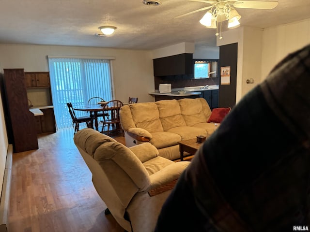 living room featuring a textured ceiling, light wood-type flooring, a wealth of natural light, and ceiling fan