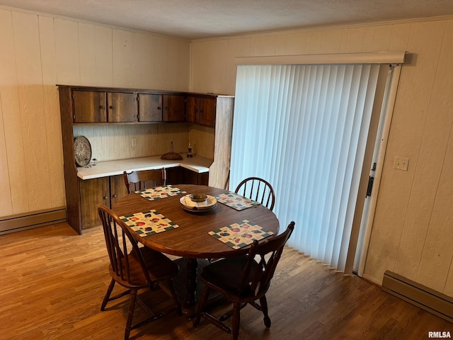 dining room with light wood-type flooring, baseboard heating, and wood walls