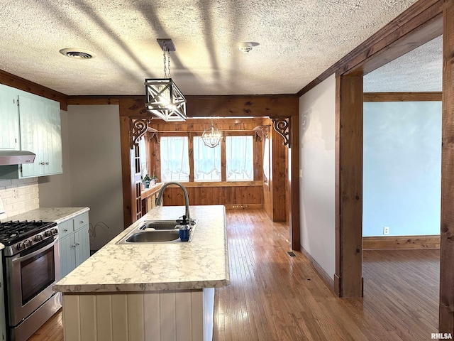 kitchen featuring gas stove, extractor fan, sink, hanging light fixtures, and an island with sink