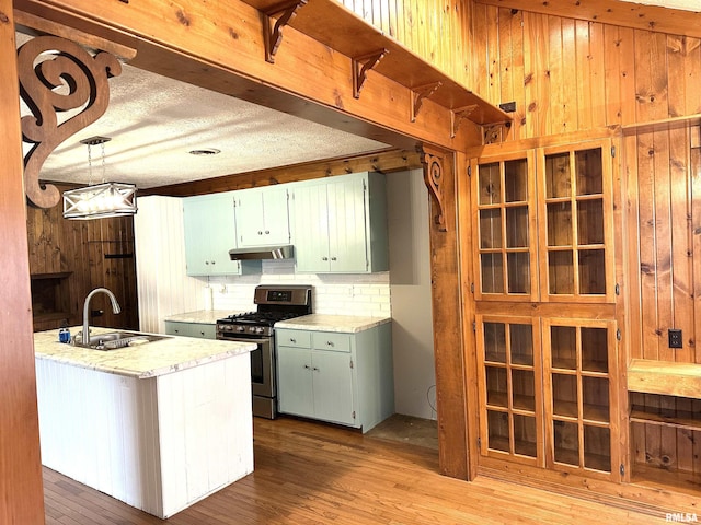 kitchen with decorative backsplash, gas stove, sink, pendant lighting, and light hardwood / wood-style floors