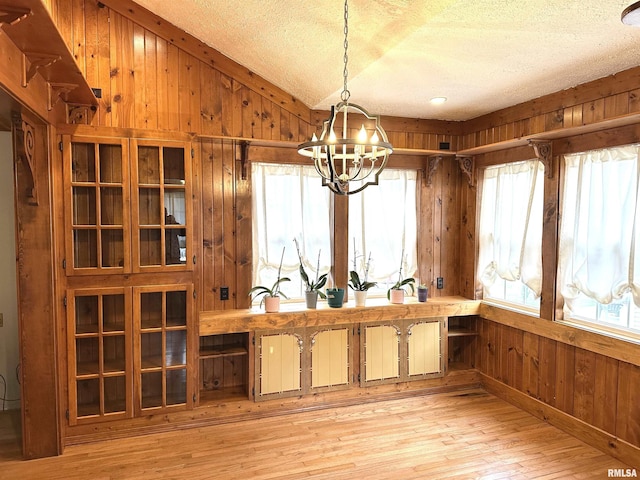 interior space with a textured ceiling, light hardwood / wood-style floors, an inviting chandelier, and wooden walls