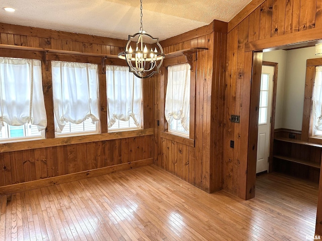 unfurnished dining area with wood walls, a notable chandelier, a textured ceiling, and hardwood / wood-style flooring