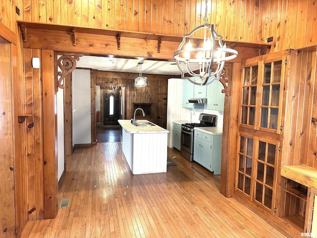 kitchen with hardwood / wood-style floors, stainless steel gas range oven, a kitchen island with sink, sink, and hanging light fixtures