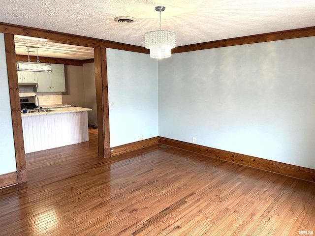 unfurnished dining area featuring a textured ceiling, sink, beam ceiling, hardwood / wood-style flooring, and a notable chandelier