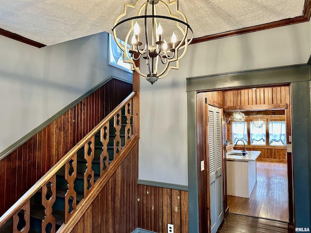 staircase featuring ornamental molding, a textured ceiling, hardwood / wood-style flooring, a notable chandelier, and wood walls