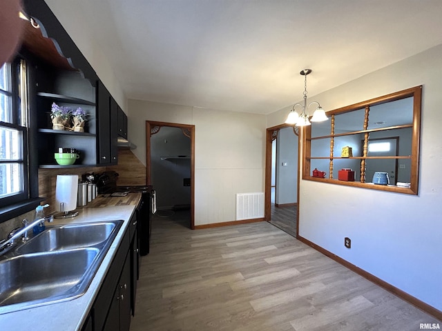 kitchen featuring black range oven, sink, hanging light fixtures, light hardwood / wood-style floors, and an inviting chandelier