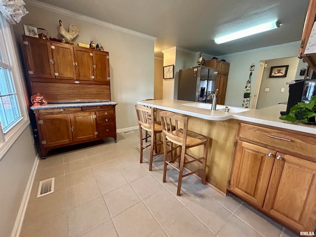 kitchen with sink, stainless steel refrigerator with ice dispenser, a breakfast bar, light tile patterned flooring, and ornamental molding