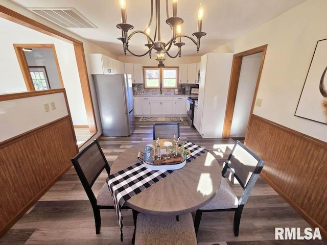 dining room featuring wood walls, dark hardwood / wood-style floors, and an inviting chandelier