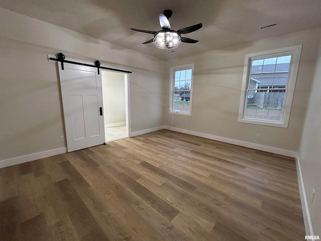 unfurnished bedroom featuring hardwood / wood-style floors, a barn door, and ceiling fan