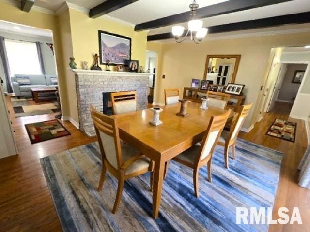 dining room featuring dark hardwood / wood-style floors, ornamental molding, a fireplace, beam ceiling, and a chandelier