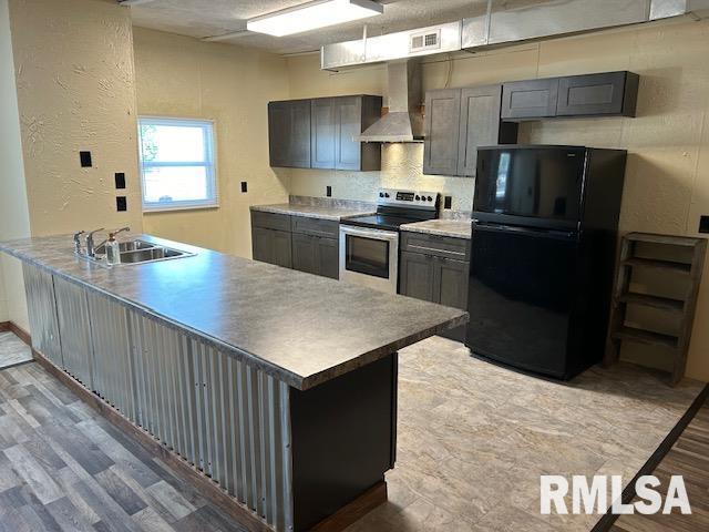 kitchen featuring black refrigerator, wall chimney range hood, sink, stainless steel electric range oven, and light hardwood / wood-style floors