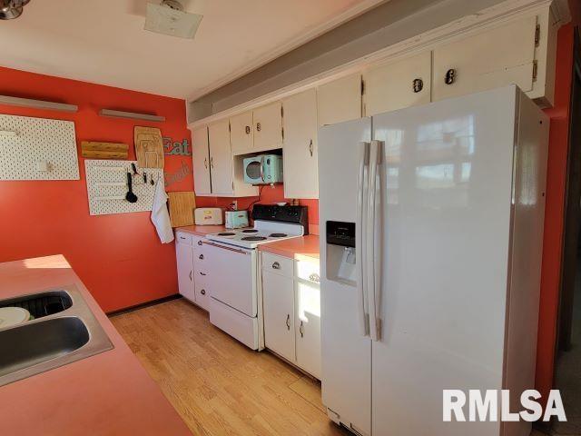 kitchen featuring white appliances, white cabinets, light countertops, light wood-style floors, and a sink