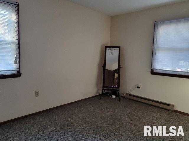 spare room with dark colored carpet, baseboards, a healthy amount of sunlight, and baseboard heating