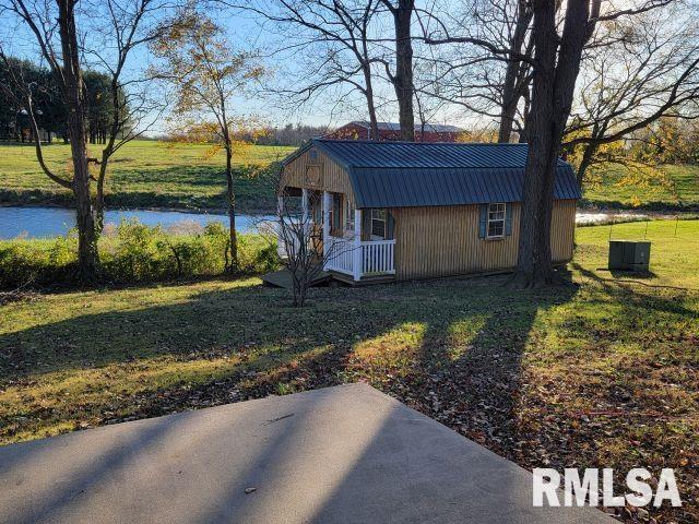 view of property exterior featuring a lawn, a patio area, an outbuilding, and a water view