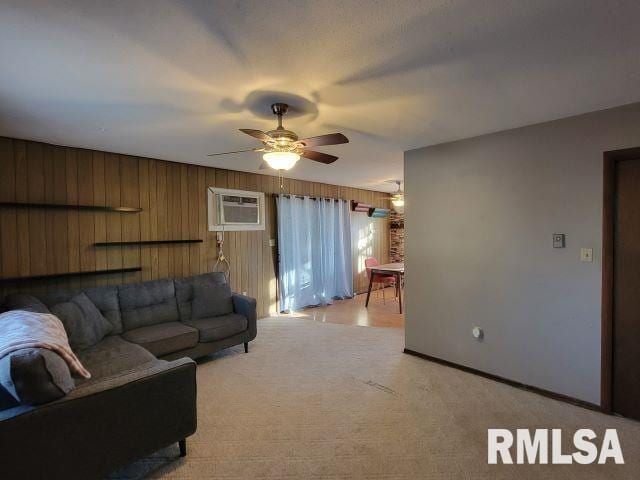 living room featuring a wall unit AC, light carpet, wood walls, ceiling fan, and baseboards