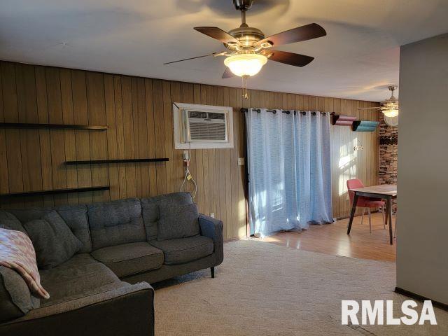 living room with light carpet, ceiling fan, a wall unit AC, and wooden walls