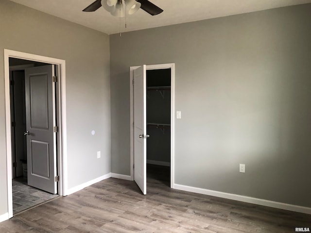 unfurnished bedroom featuring a closet, a walk in closet, ceiling fan, and hardwood / wood-style floors