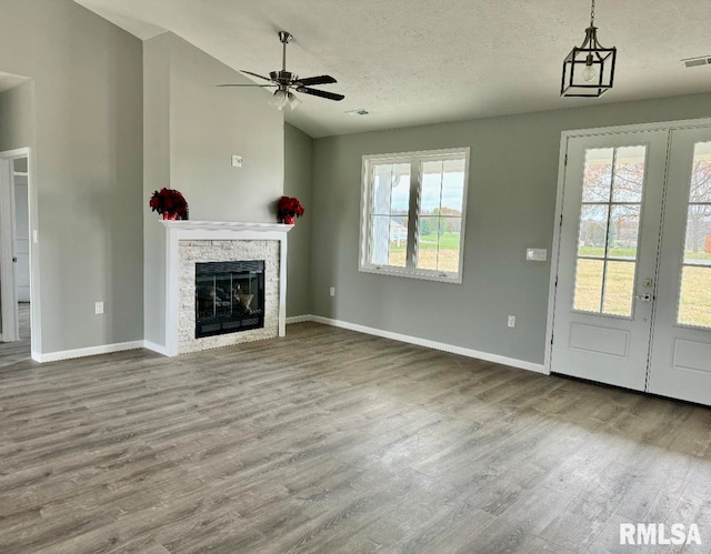 unfurnished living room featuring a textured ceiling, hardwood / wood-style flooring, a stone fireplace, and ceiling fan