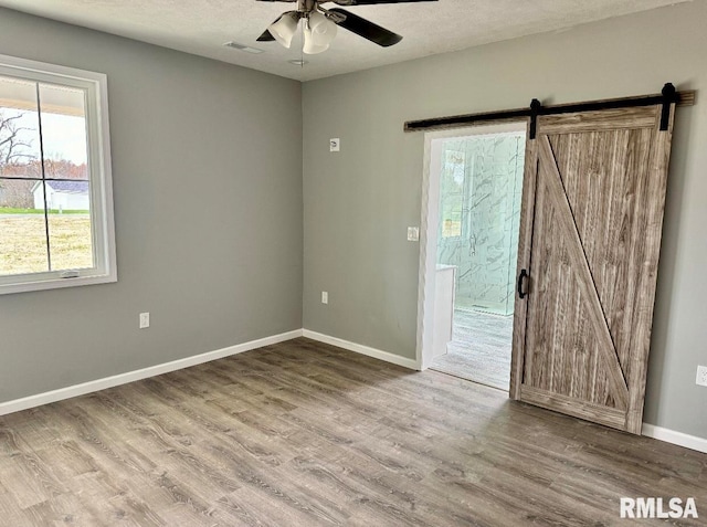 spare room featuring hardwood / wood-style floors, a barn door, a textured ceiling, and ceiling fan