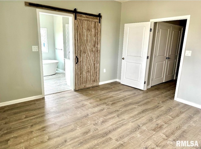 unfurnished bedroom with hardwood / wood-style flooring, a barn door, and ensuite bath