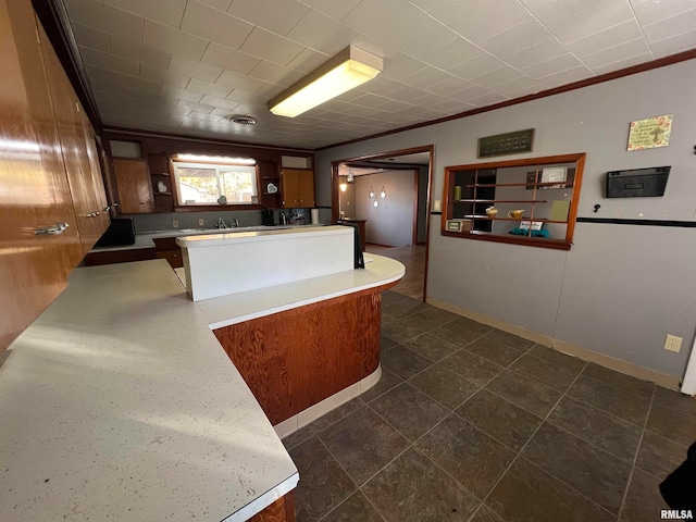 kitchen with kitchen peninsula, dark tile patterned floors, crown molding, and sink