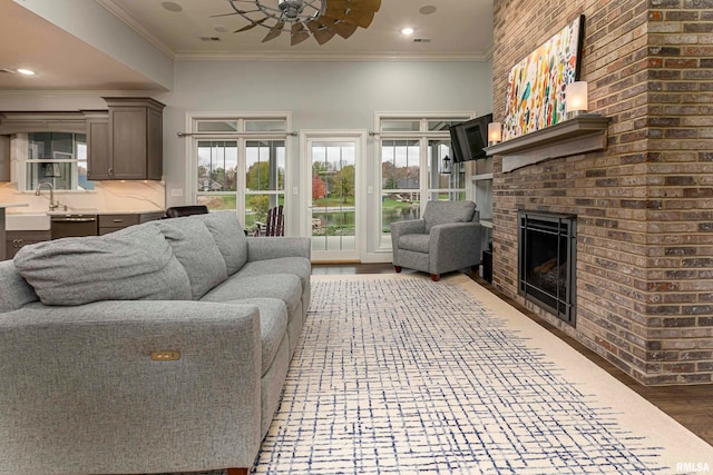 living room with a brick fireplace, ceiling fan, crown molding, and light hardwood / wood-style flooring