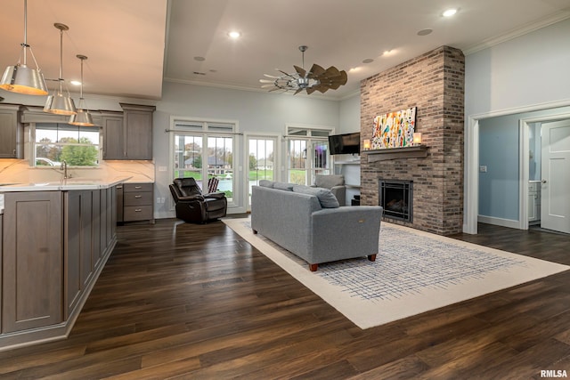 living room with ceiling fan, dark hardwood / wood-style flooring, crown molding, and a brick fireplace