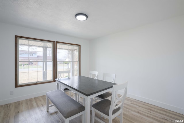 dining space featuring light wood-style floors, a textured ceiling, and baseboards