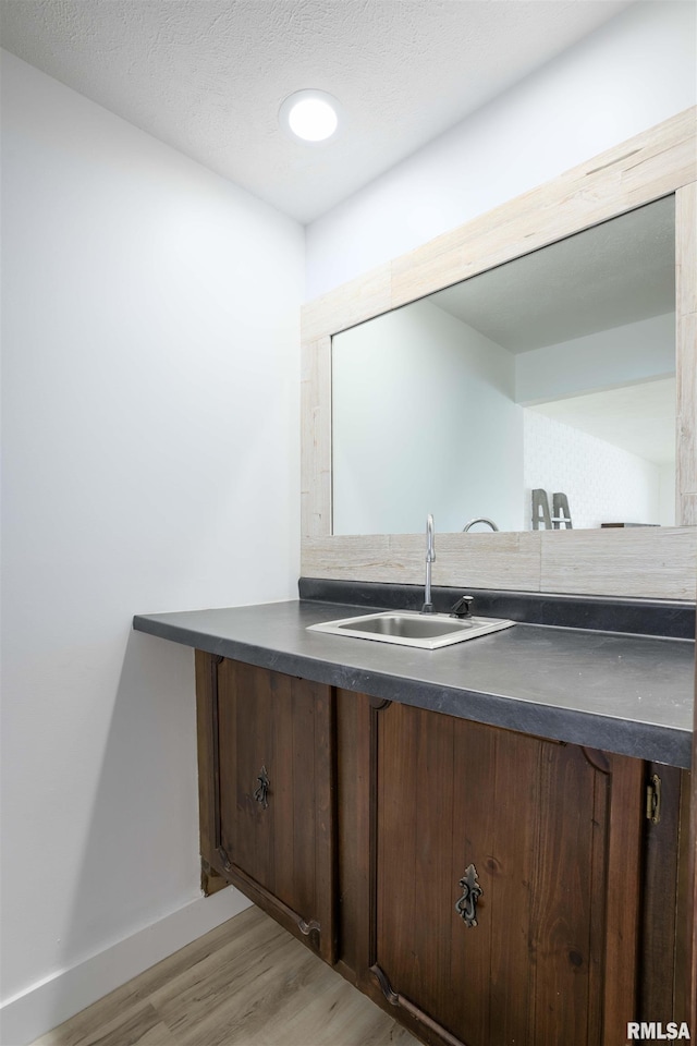 bathroom with a textured ceiling, wood finished floors, vanity, and baseboards