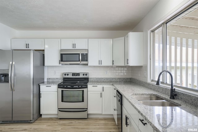 kitchen featuring white cabinets, light stone countertops, stainless steel appliances, and a sink