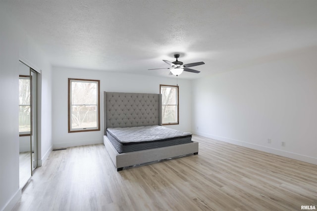 unfurnished bedroom featuring a textured ceiling, ceiling fan, light wood-type flooring, and baseboards