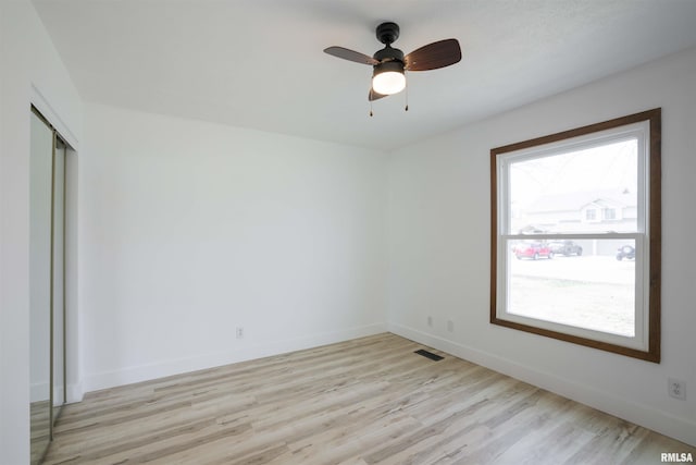 empty room featuring light wood-type flooring, baseboards, visible vents, and ceiling fan