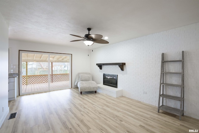 unfurnished room featuring ceiling fan, a textured ceiling, brick wall, a fireplace, and light wood-style floors